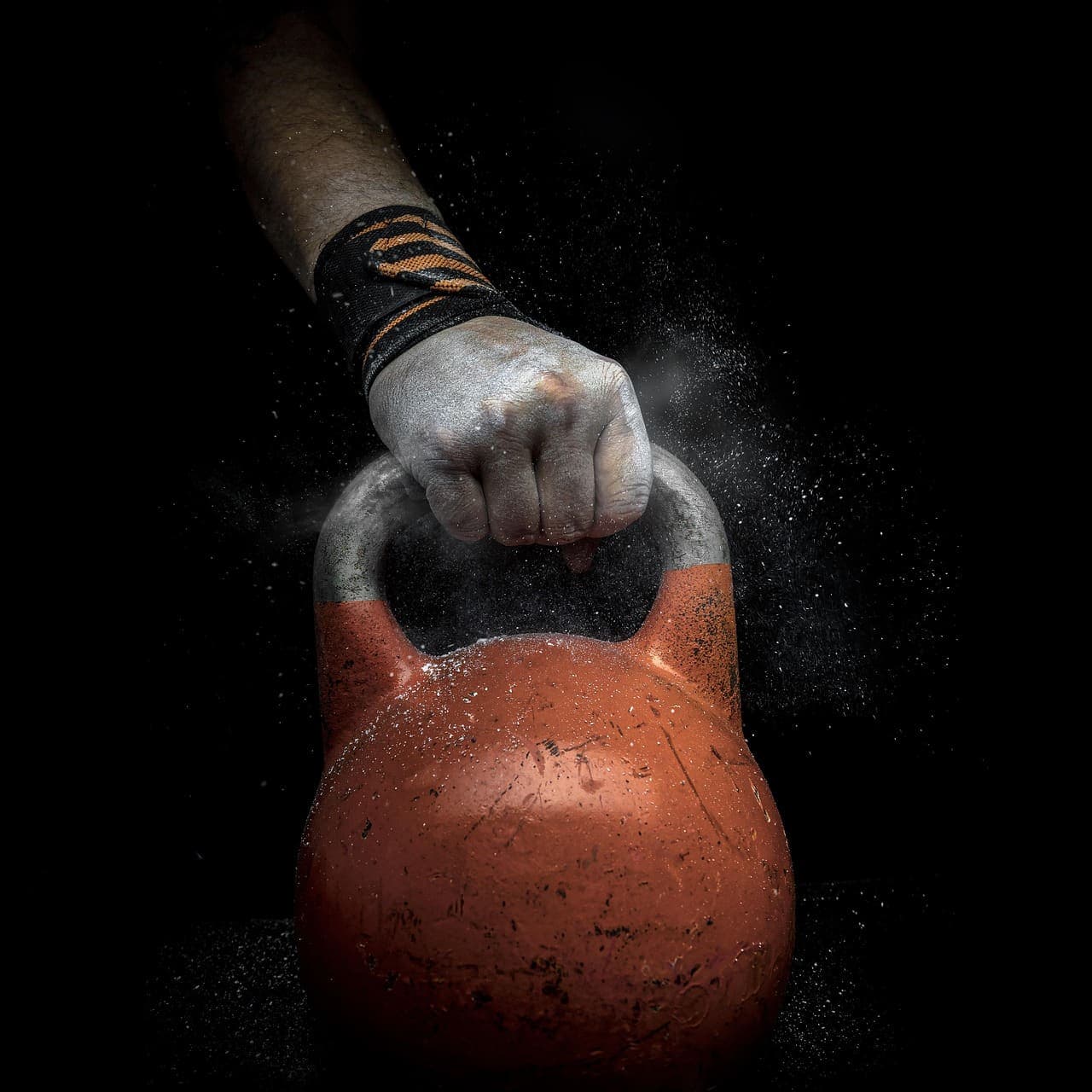 Chalked hand gripping an orange kettlebell
